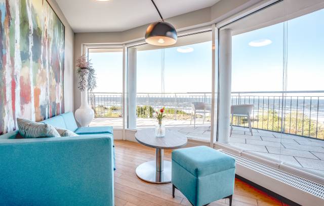 Helles Zimmer im Das Ahlbeck Hotel & Spa mit modernem Sofa, bodentiefen Fenstern und Panoramablick auf die Ostsee vom Balkon